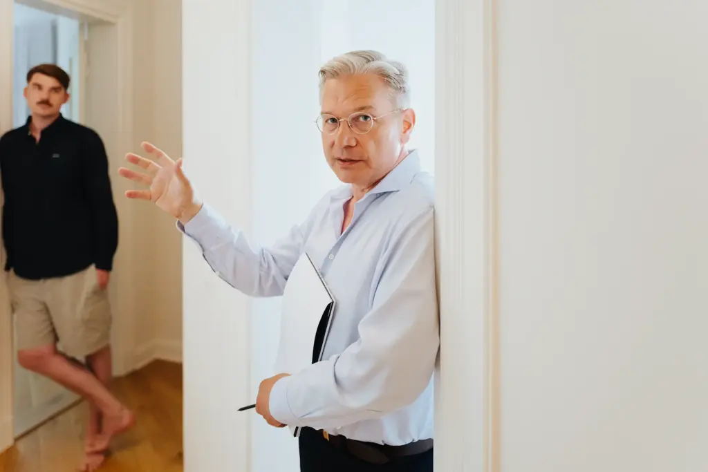 Ulrich Weinkath bespricht sich mit einem männlichen Kunden in einem Flur. Es handelt sich um eine Klientenwohnung.