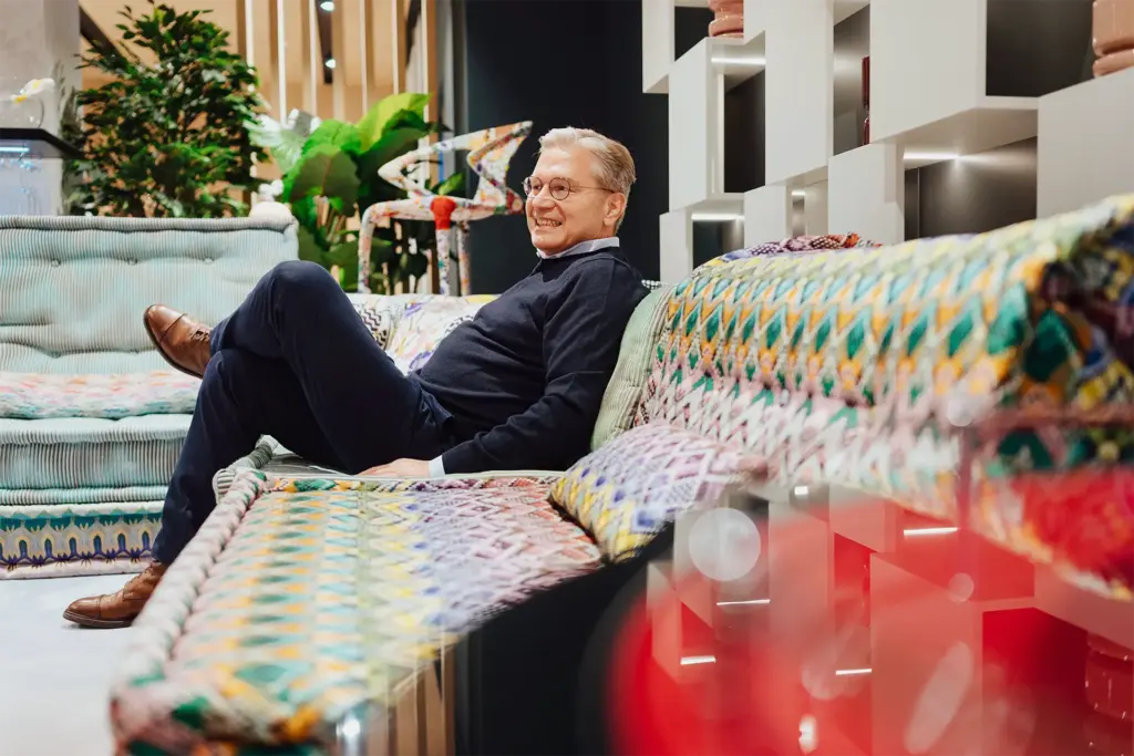 Ulrich Weinkath sitzt auf einem buntem Sofa in einem Interior-Showroom am Neuen Wall. Er lächelt.
